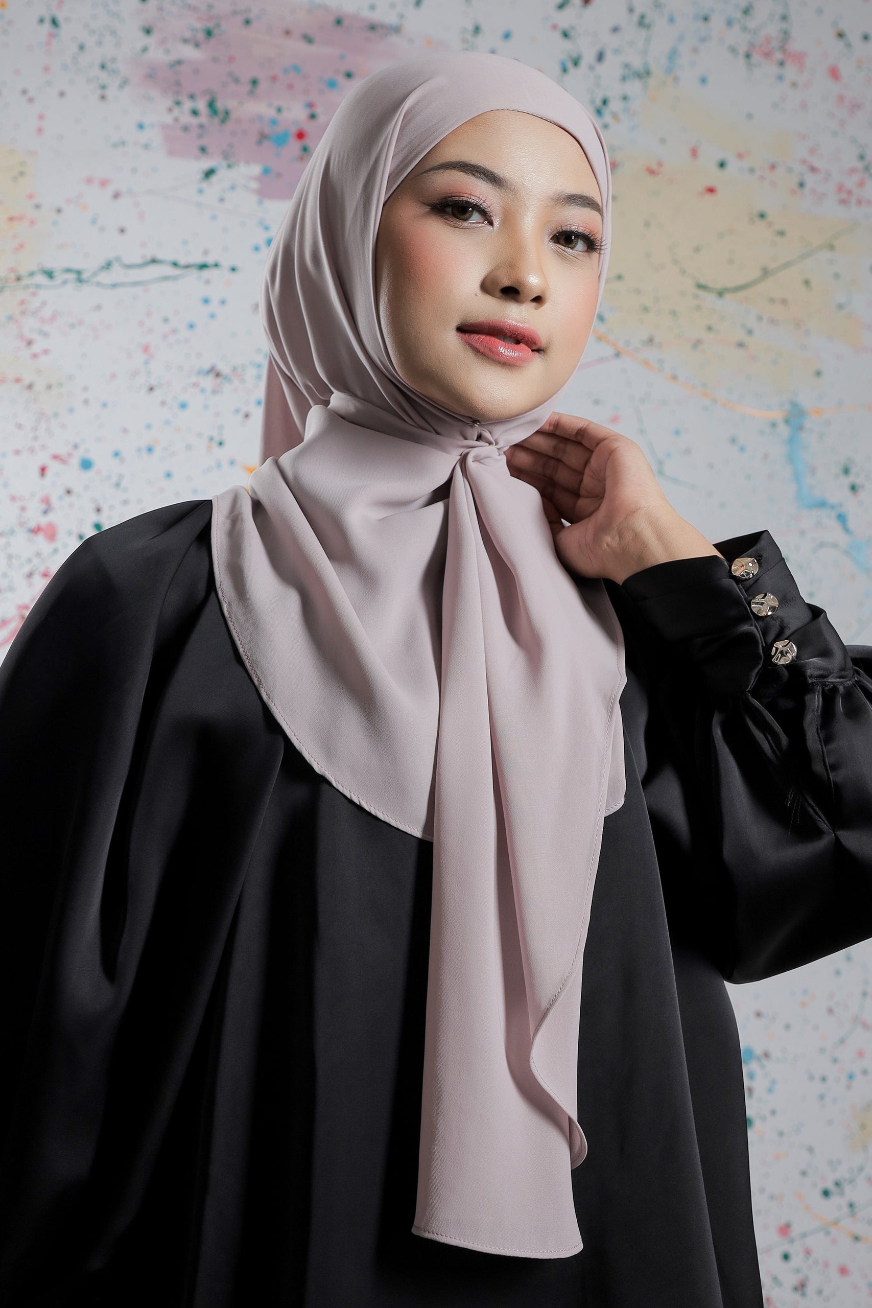 Woman wearing a light pink hijab and black outfit against a colorful abstract background