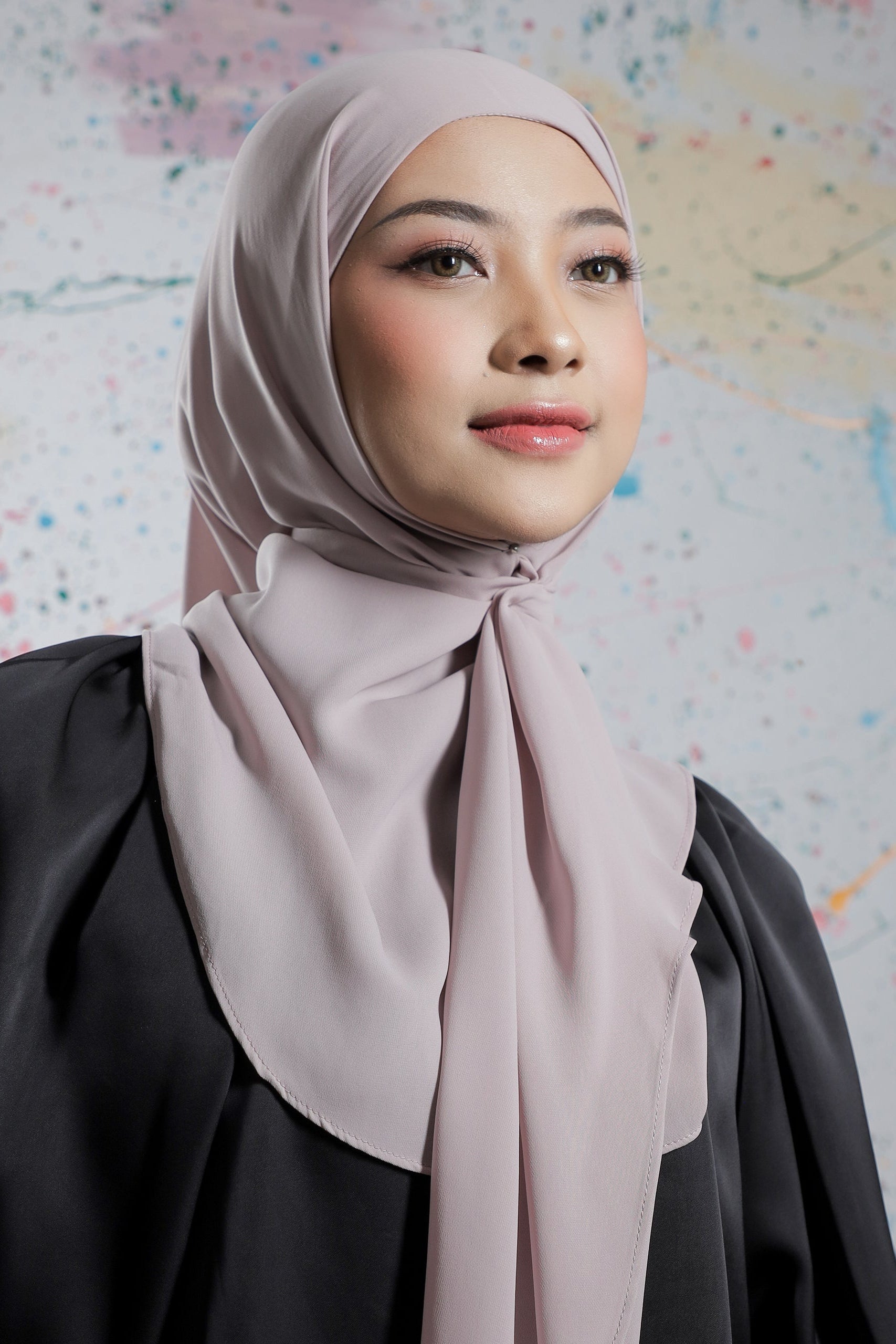 Woman wearing a light pink hijab and black outfit against a colorful abstract background