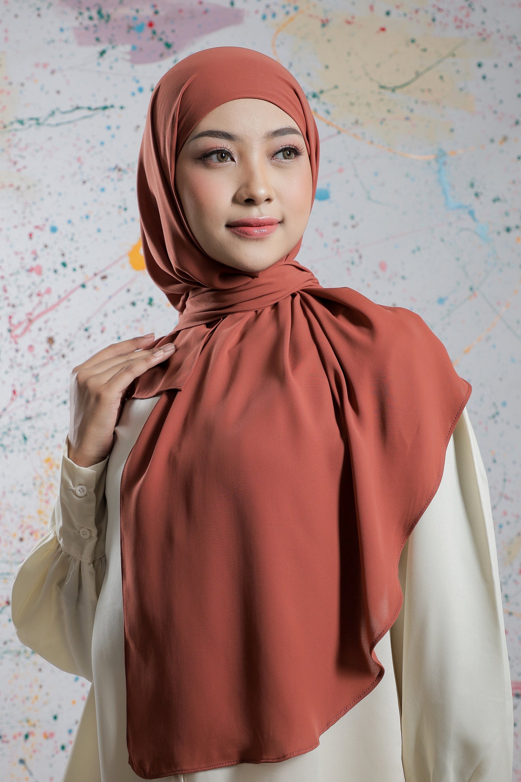 Woman wearing a rust-colored hijab against a colorful abstract background
