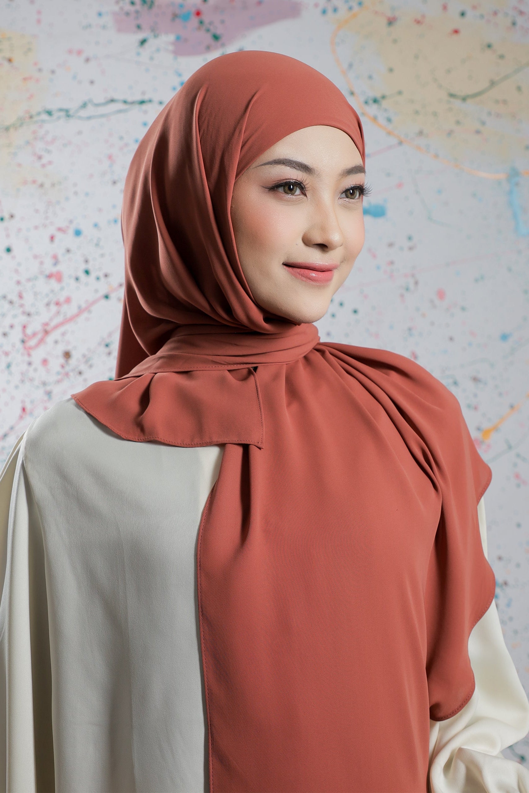 Woman wearing a rust-colored hijab against a colorful abstract background