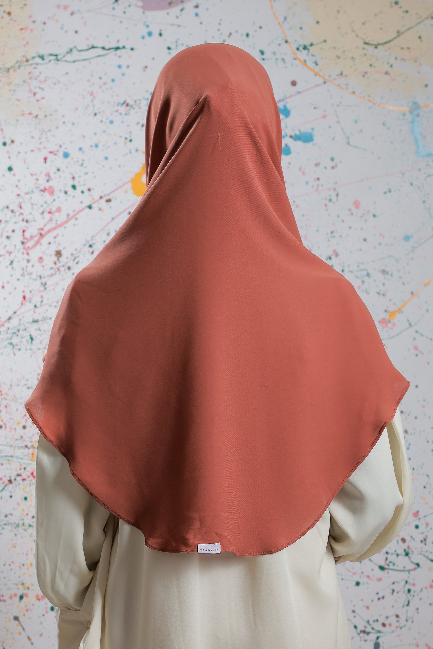 Person wearing a brown hijab and beige outfit against a colorful abstract background