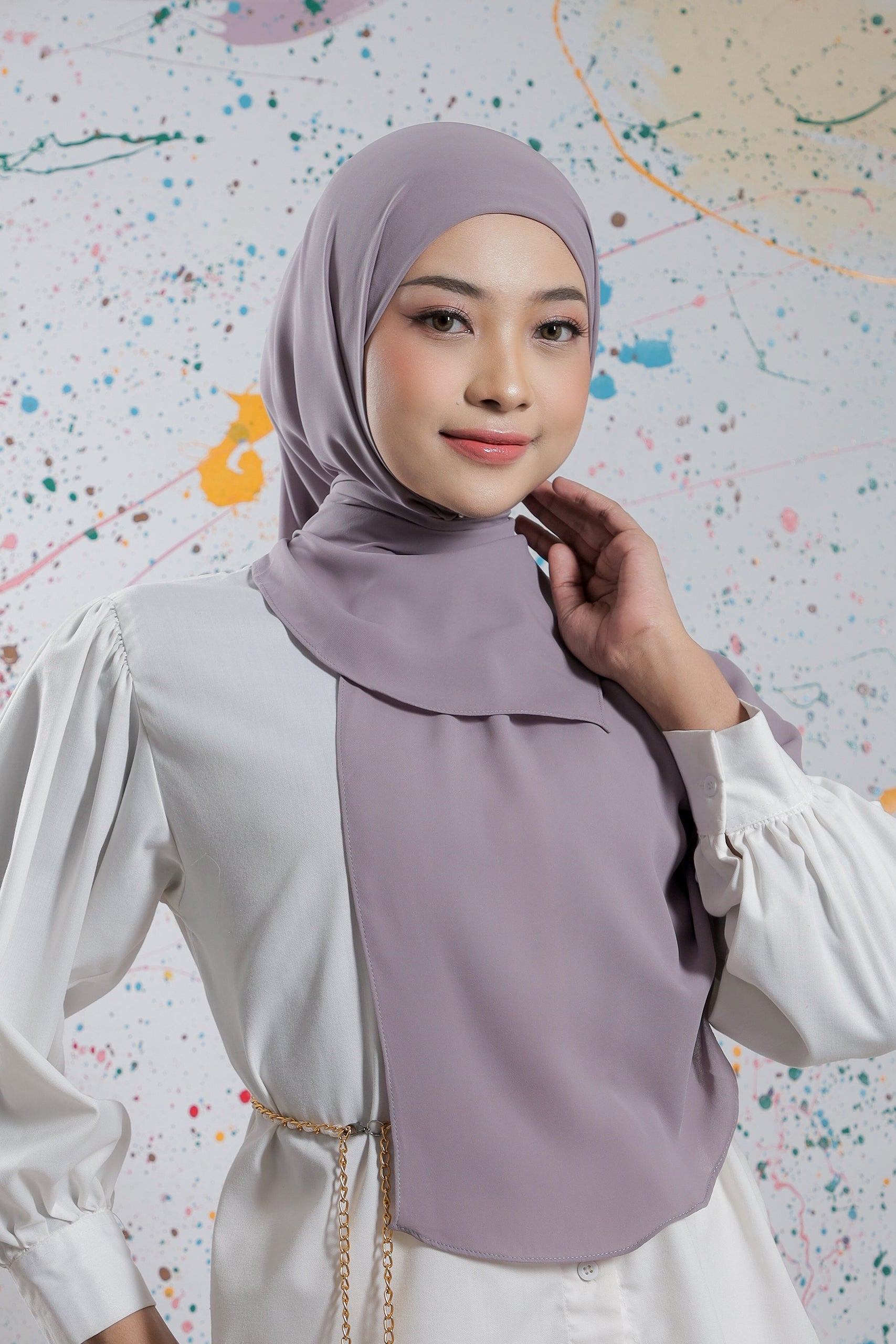 Woman wearing a light purple hijab and white blouse against a colorful abstract background