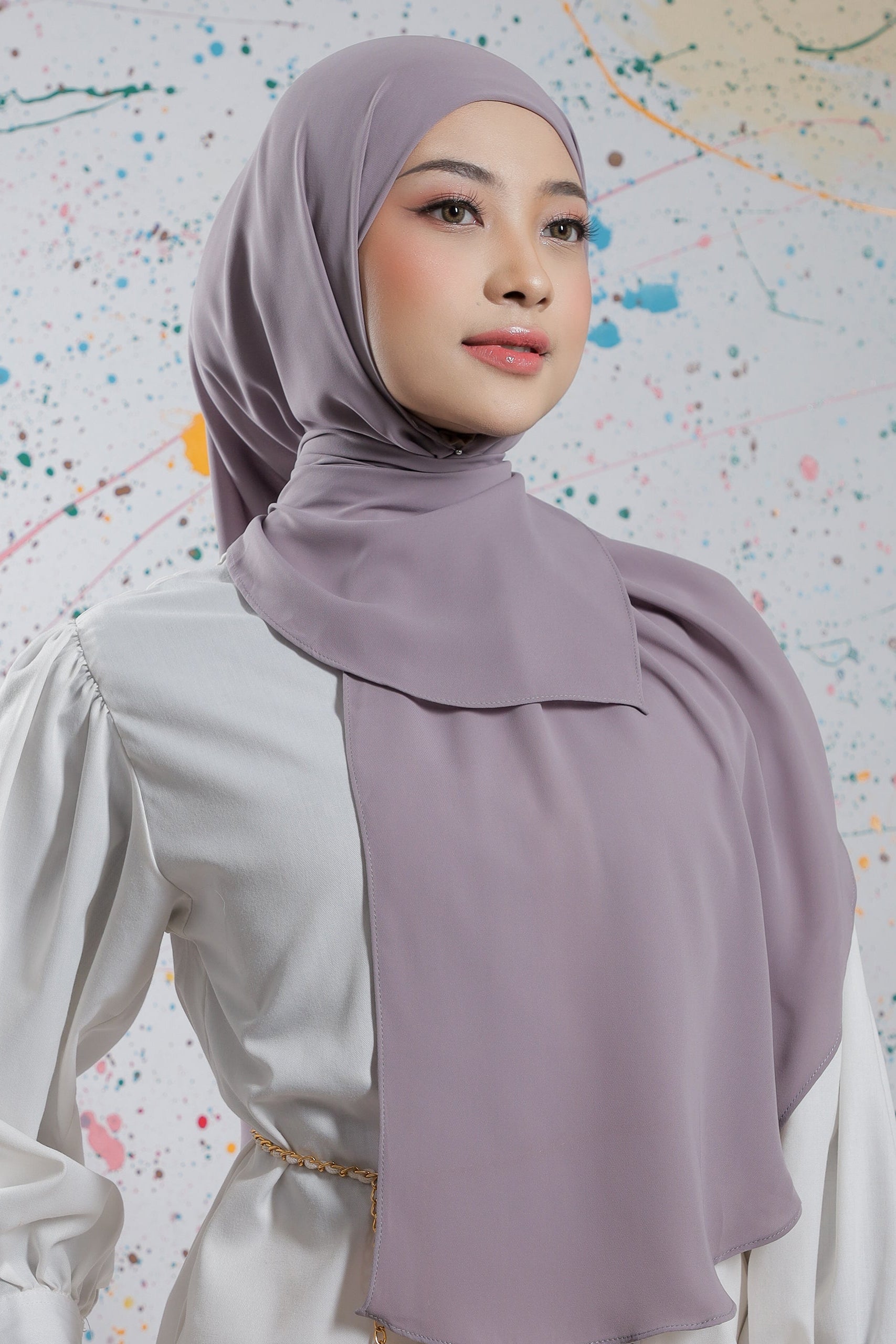 Woman wearing a light purple hijab against a colorful abstract background