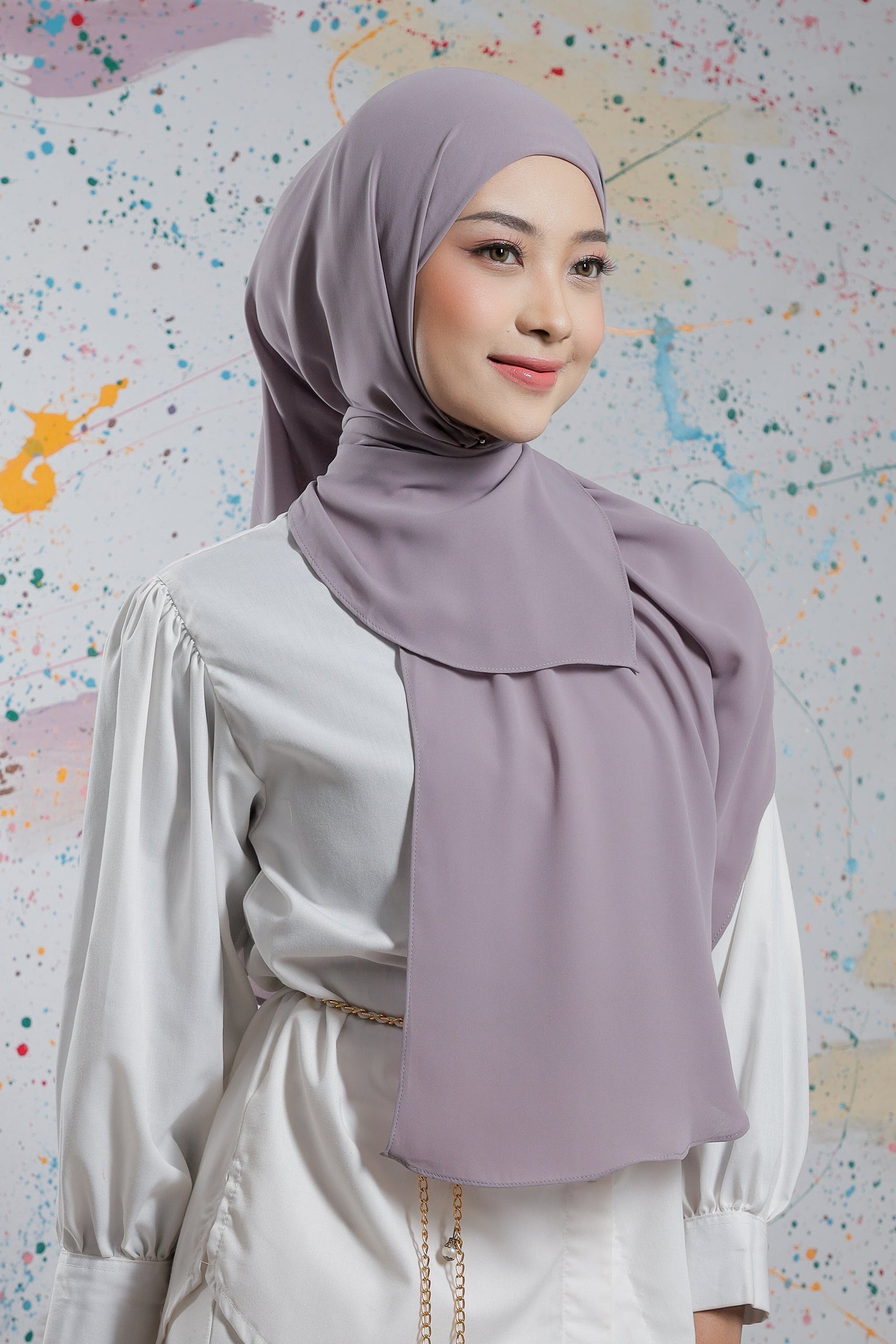 Woman wearing a light purple hijab and white outfit against a colorful abstract background