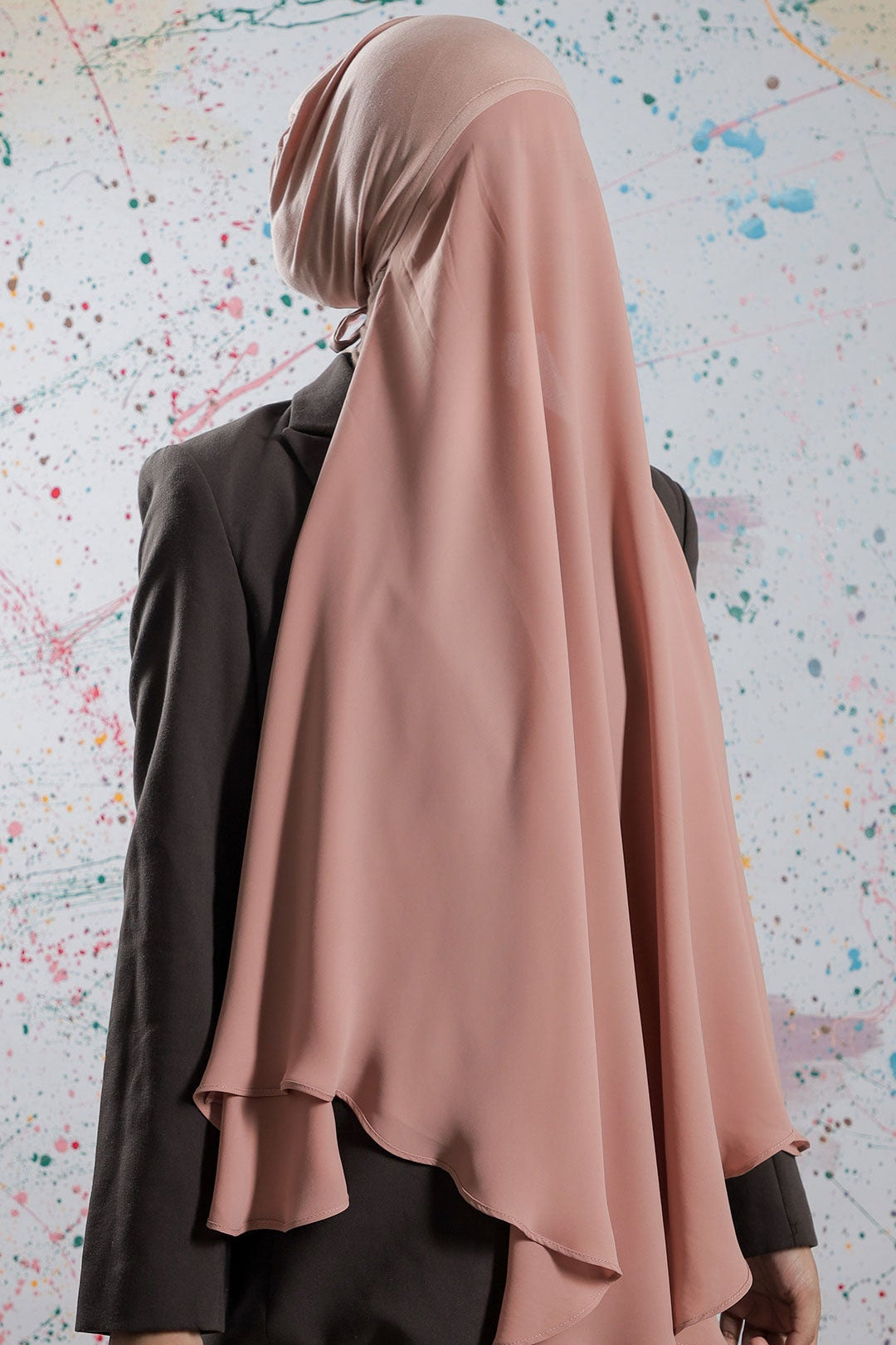 Person wearing a beige hijab and dark clothing against a colorful abstract background