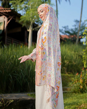 Woman wearing a floral hijab and white outfit in a garden setting