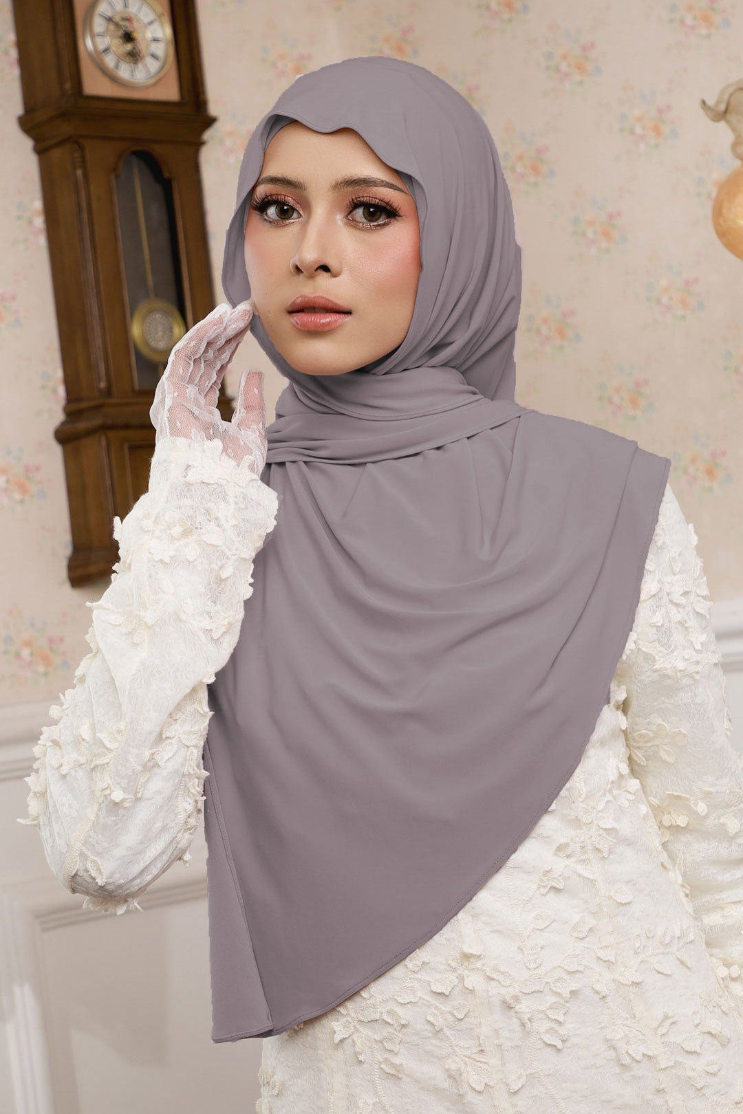 Woman wearing a gray hijab and white gloves in a decorated room with a clock.