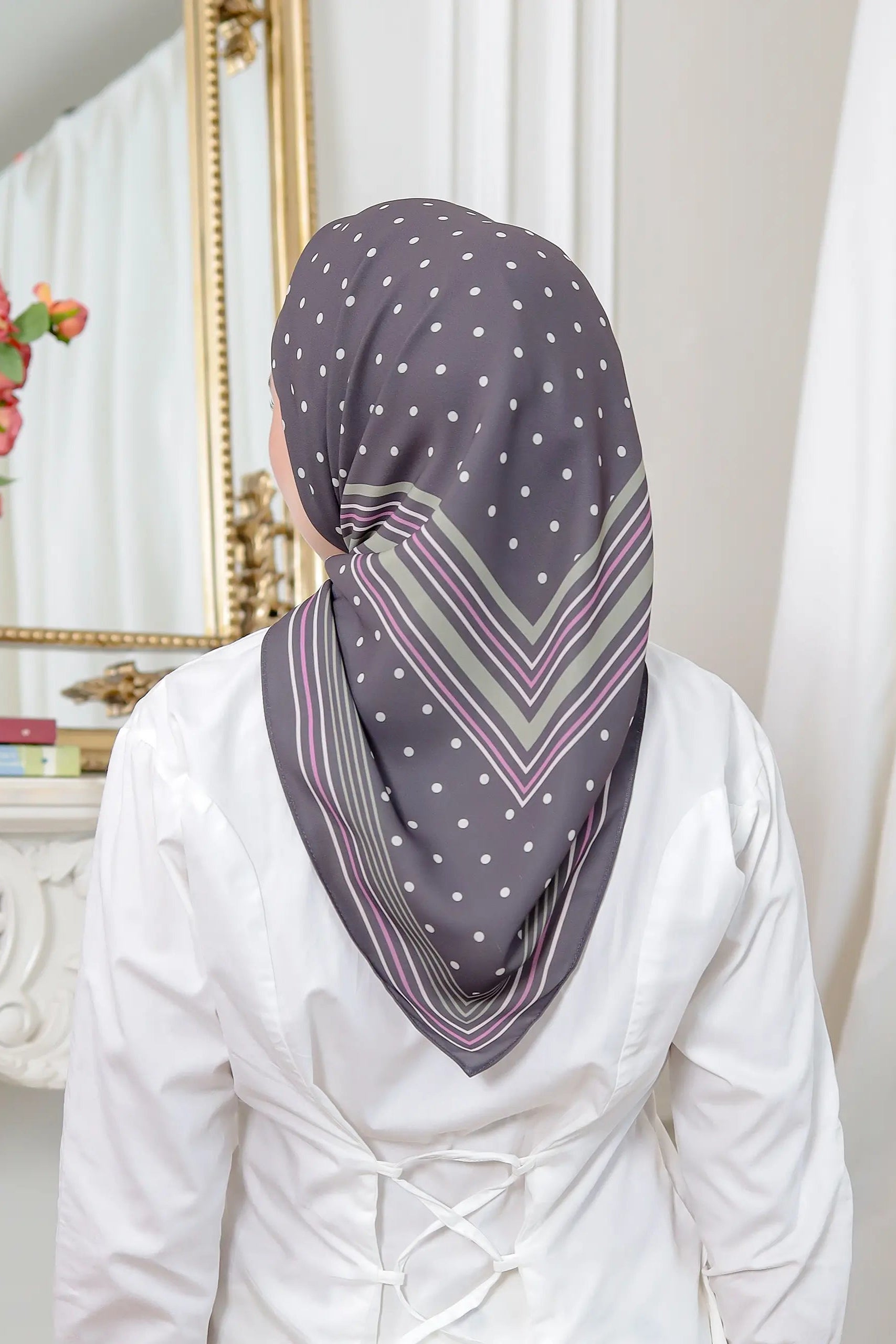 Person wearing a patterned headscarf in a room with decor elements.