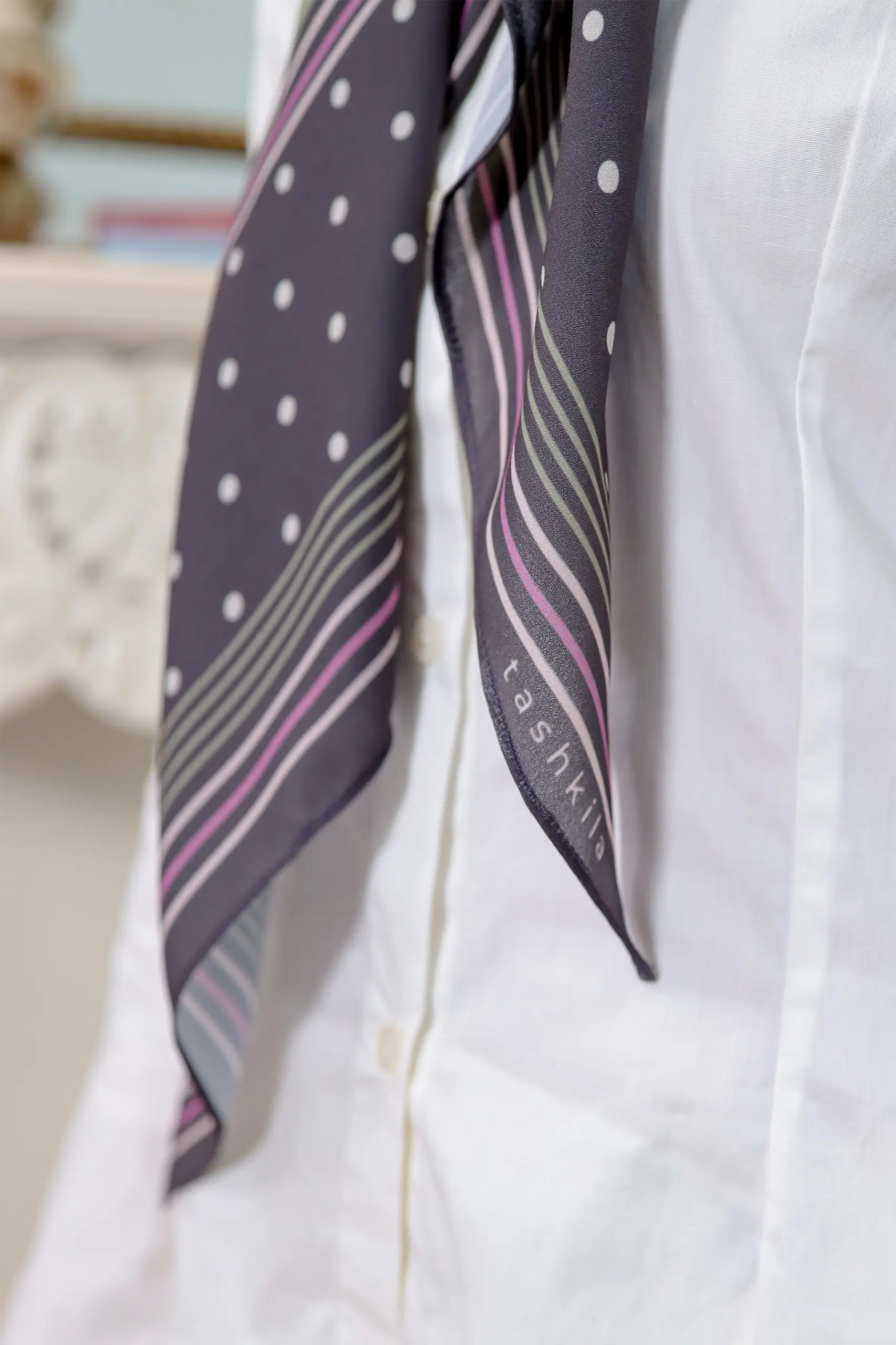 Polka dot and striped scarf draped over a white shirt with 'tasha' branding.