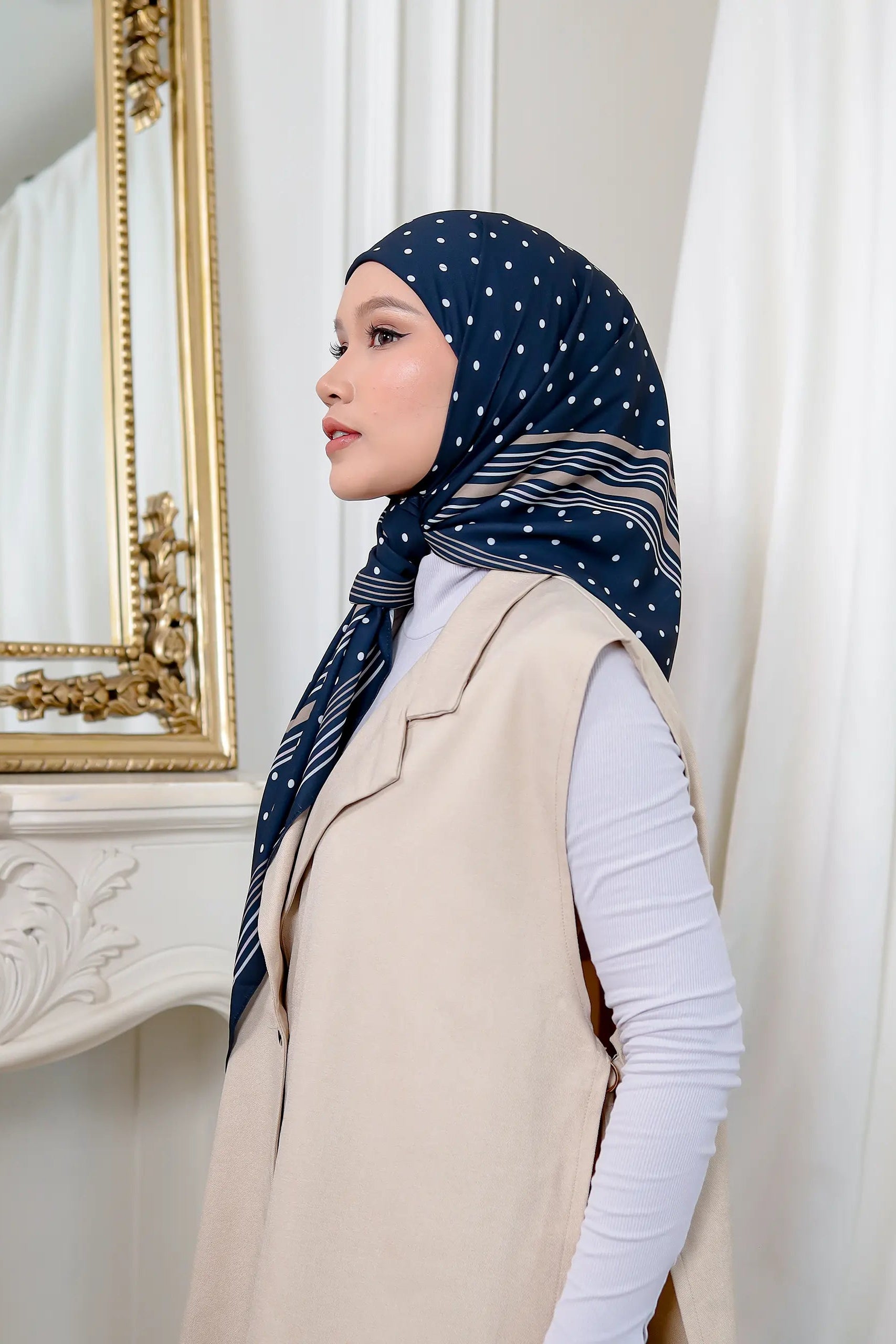 Woman wearing a navy hijab with white patterns in an elegant room.