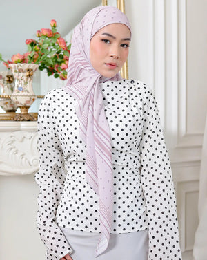 Woman wearing a polka dot blouse and hijab in a decorated room.