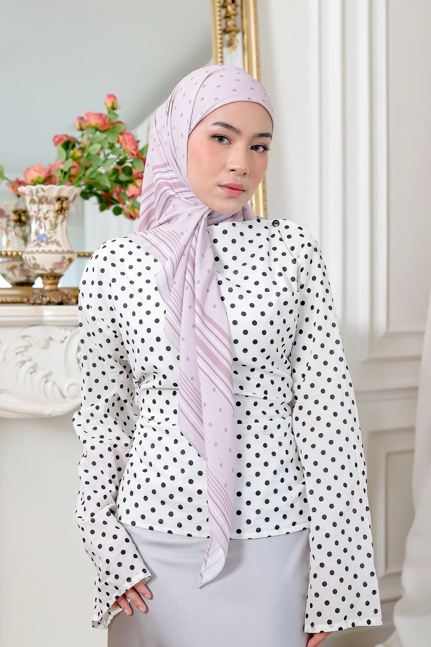 Woman wearing a polka dot blouse and hijab in a decorated room.