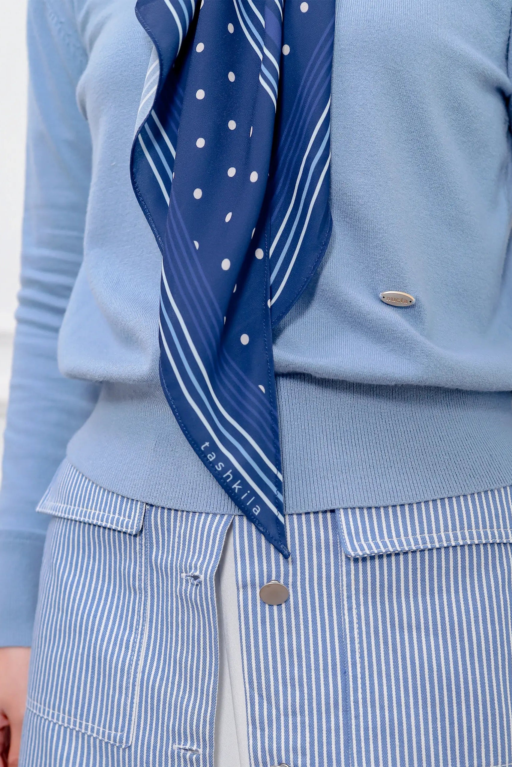 Person wearing a blue sweater and striped pants with a blue polka dot scarf.