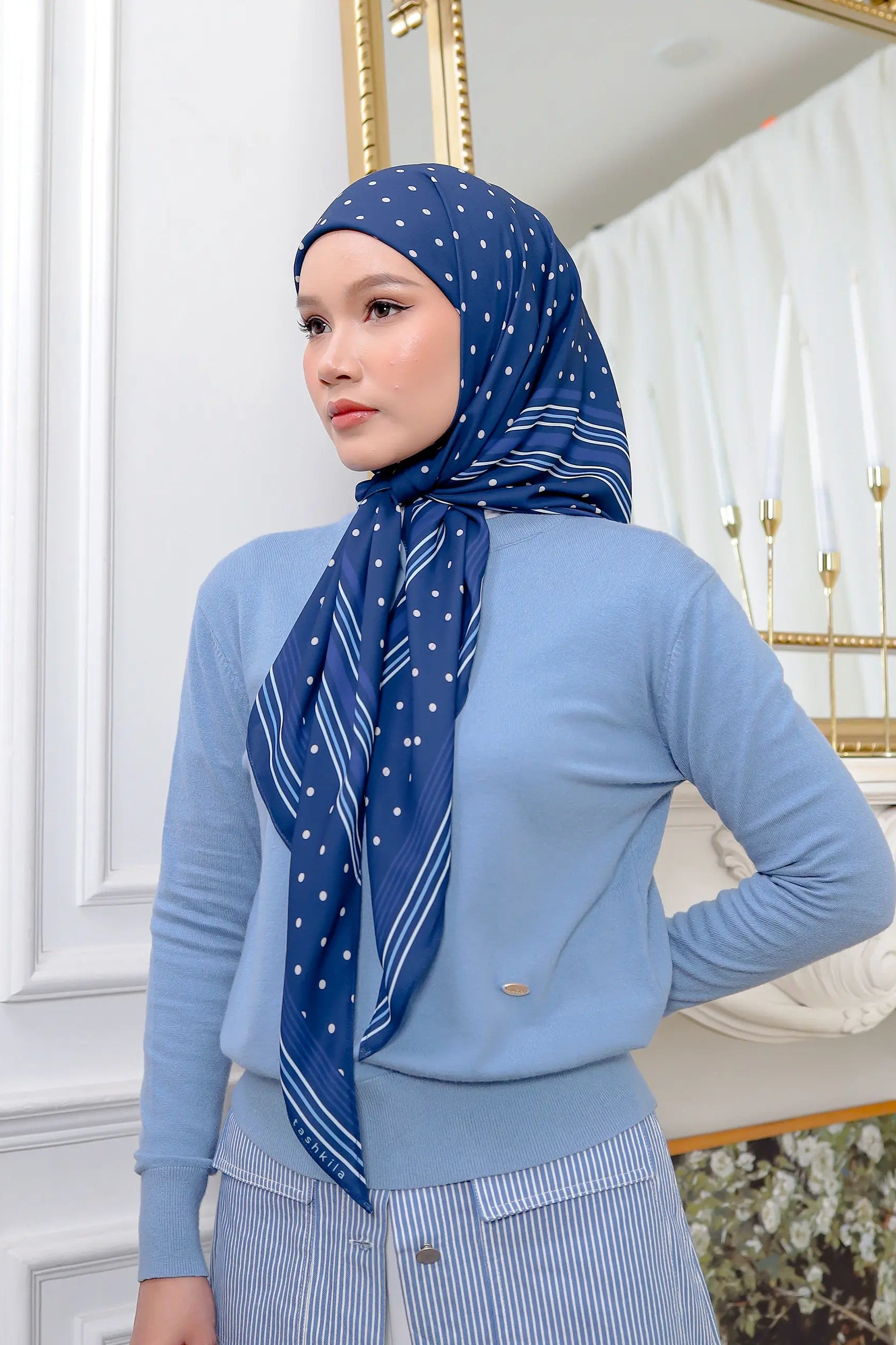 Woman wearing a blue outfit with a matching scarf in a decorative room.