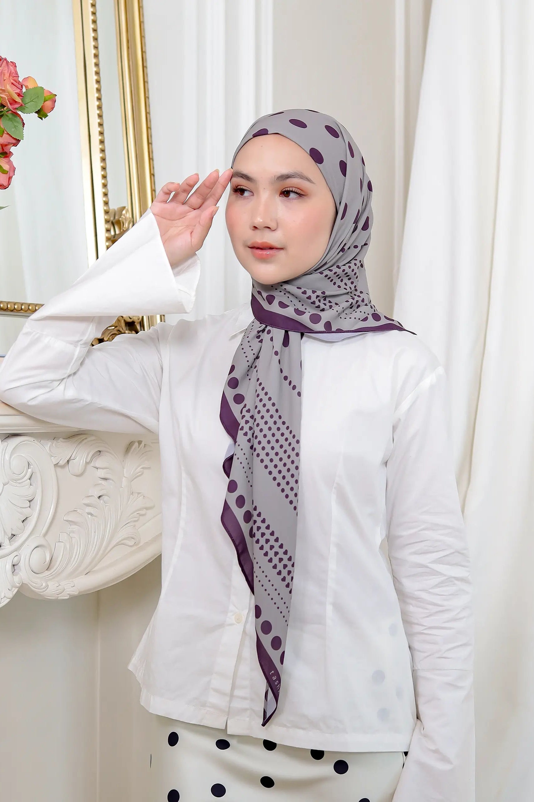 Woman wearing a patterned hijab and white outfit in a decorative setting