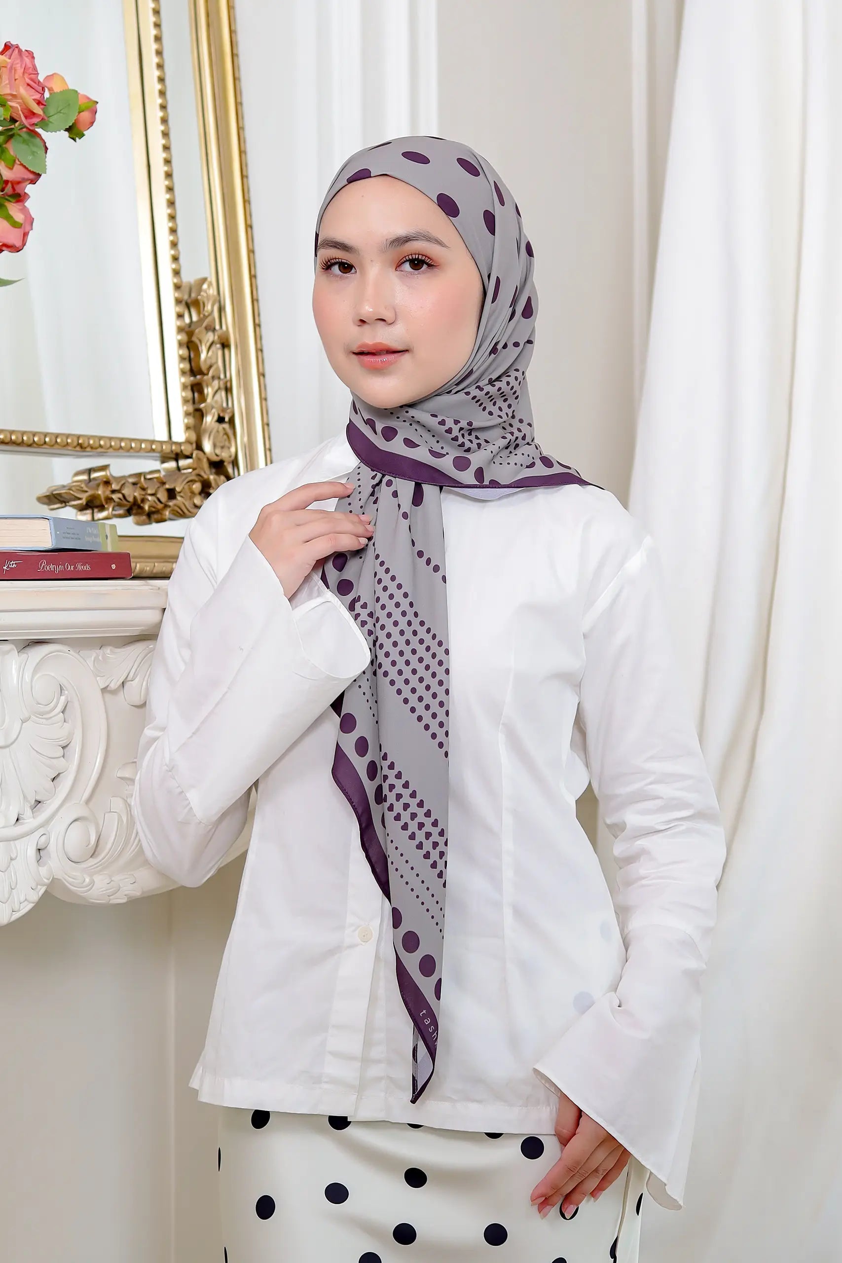 Woman wearing a white outfit with a patterned hijab in a decorative room.