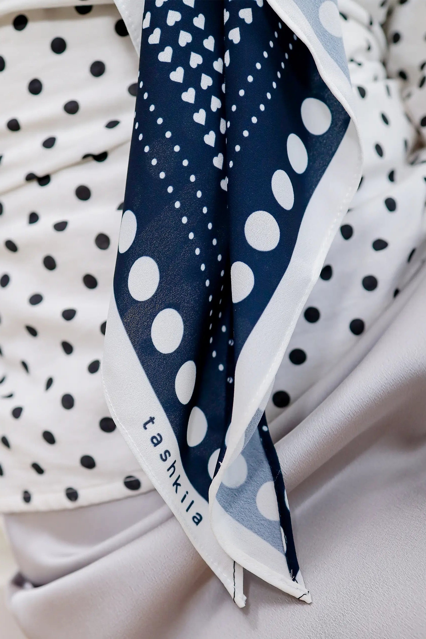 Navy blue polka dot scarf with 'tashkilla' branding draped over a white surface.