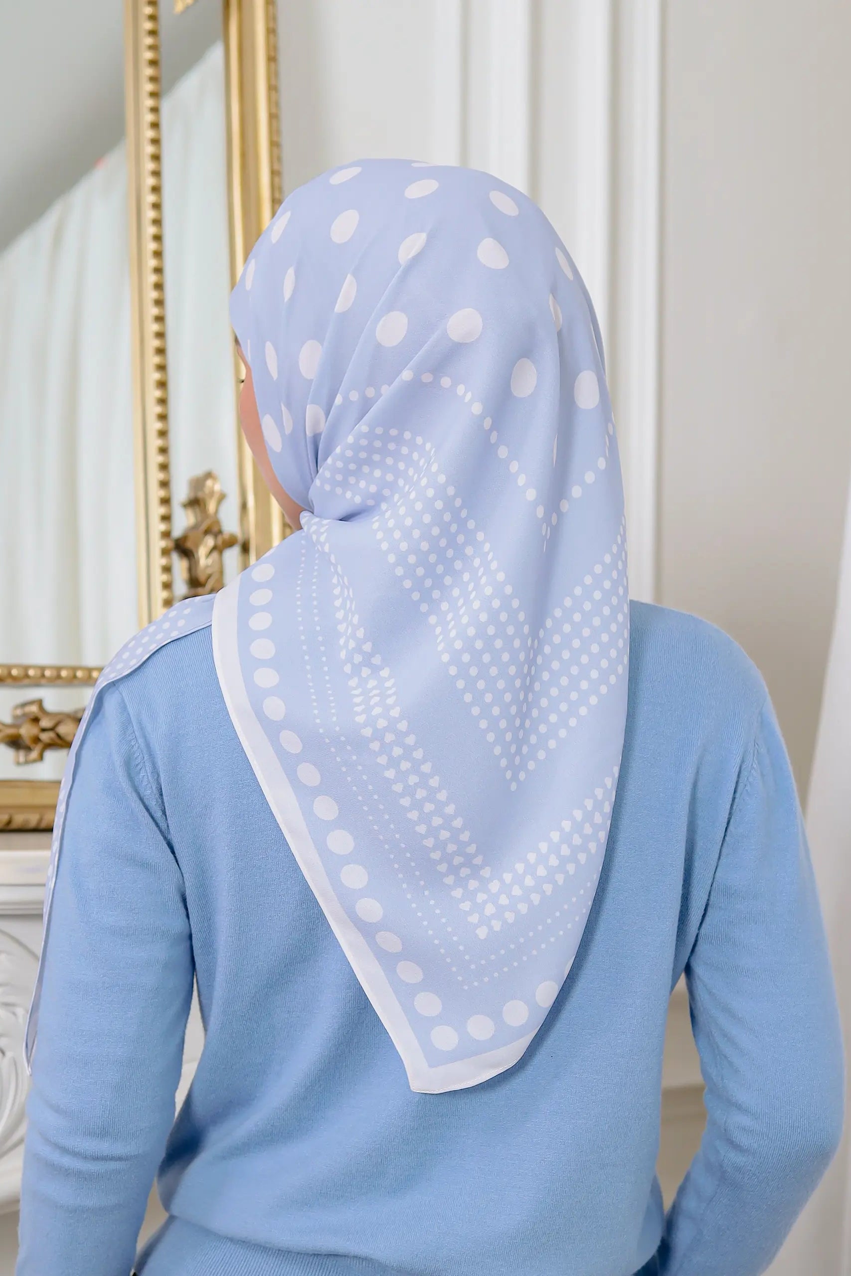 Person wearing a light blue hijab with white polka dots in a room setting.