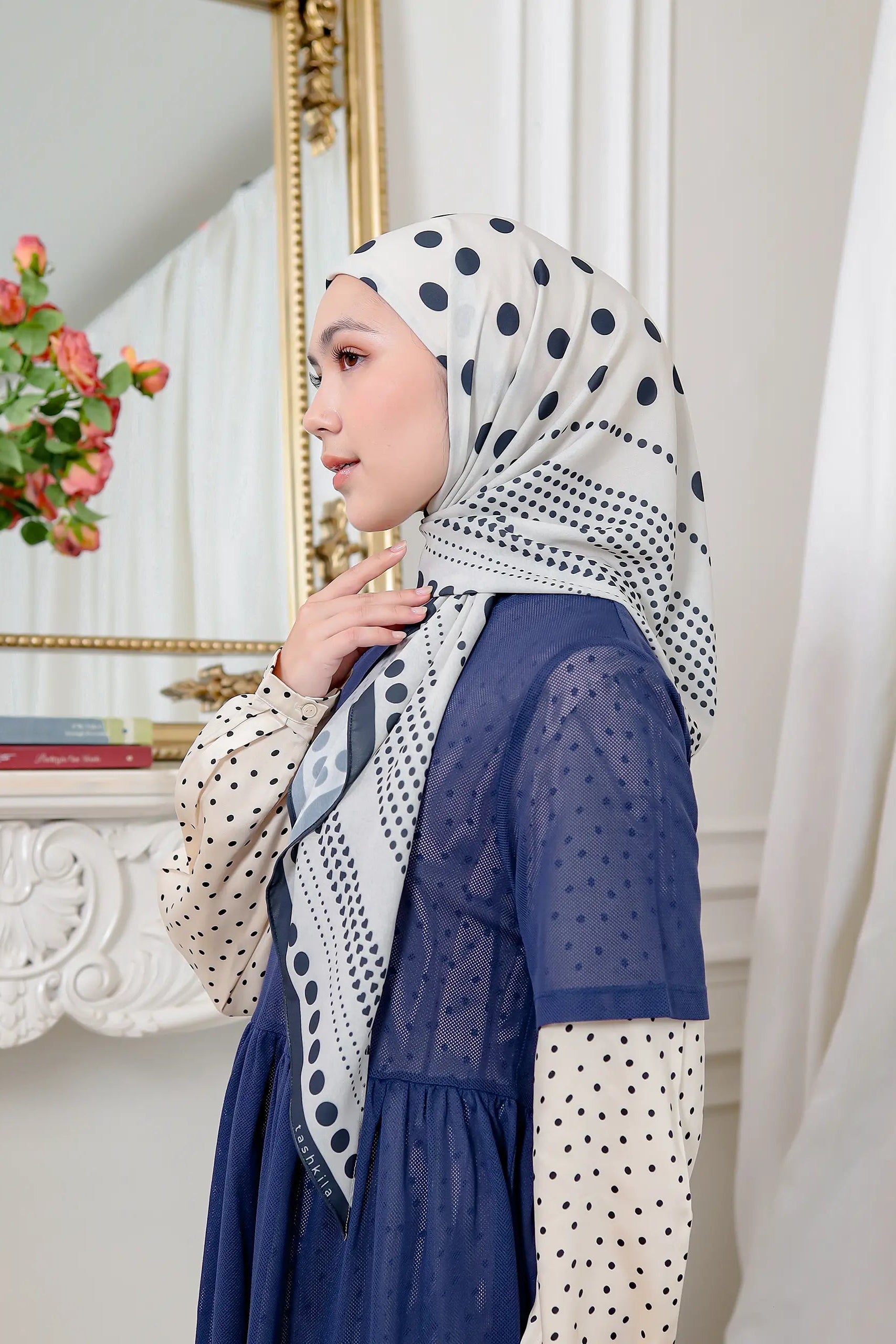 Woman wearing a patterned hijab and dress in a decorative room.