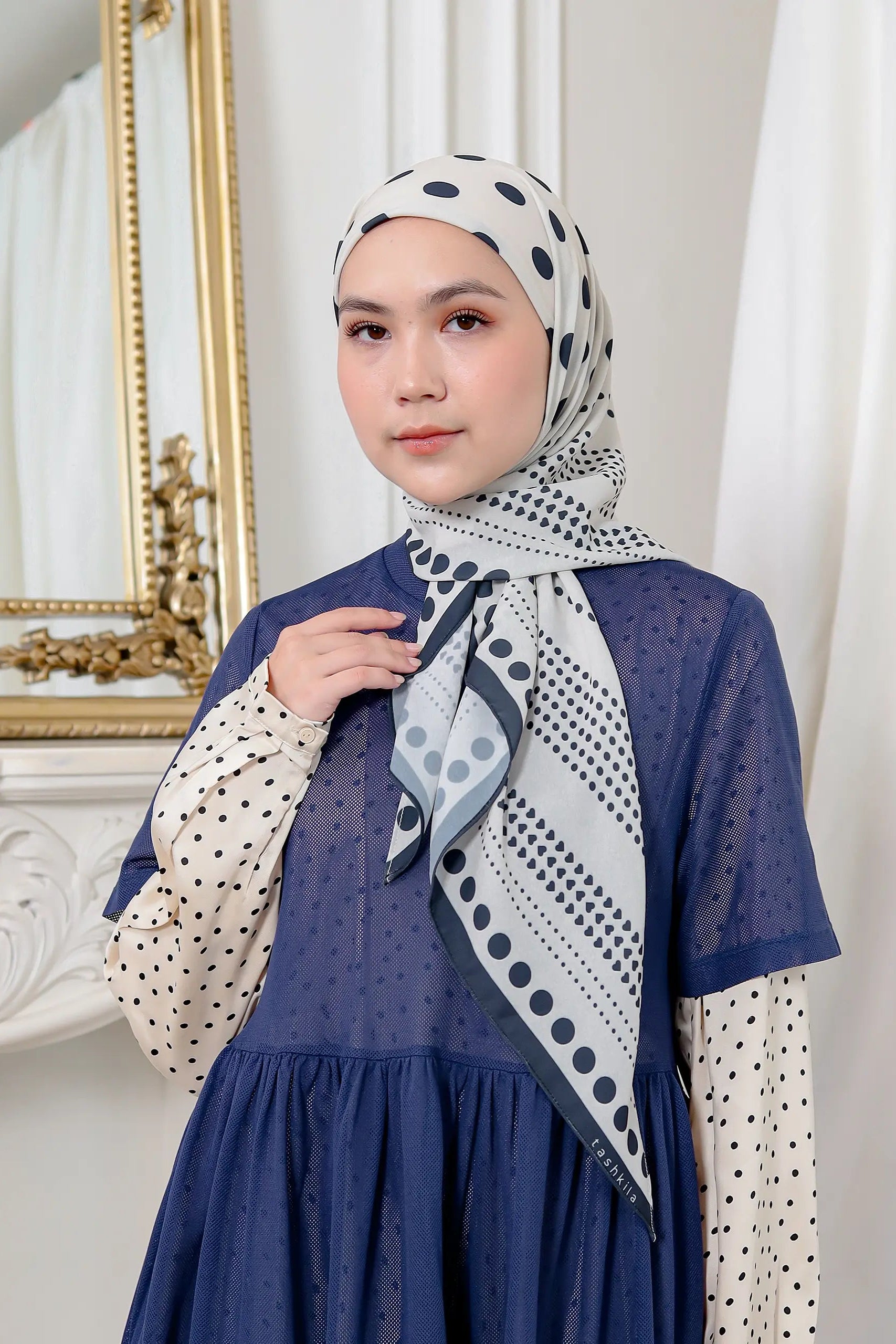 Woman wearing a blue dress with a patterned hijab in a well-lit room.