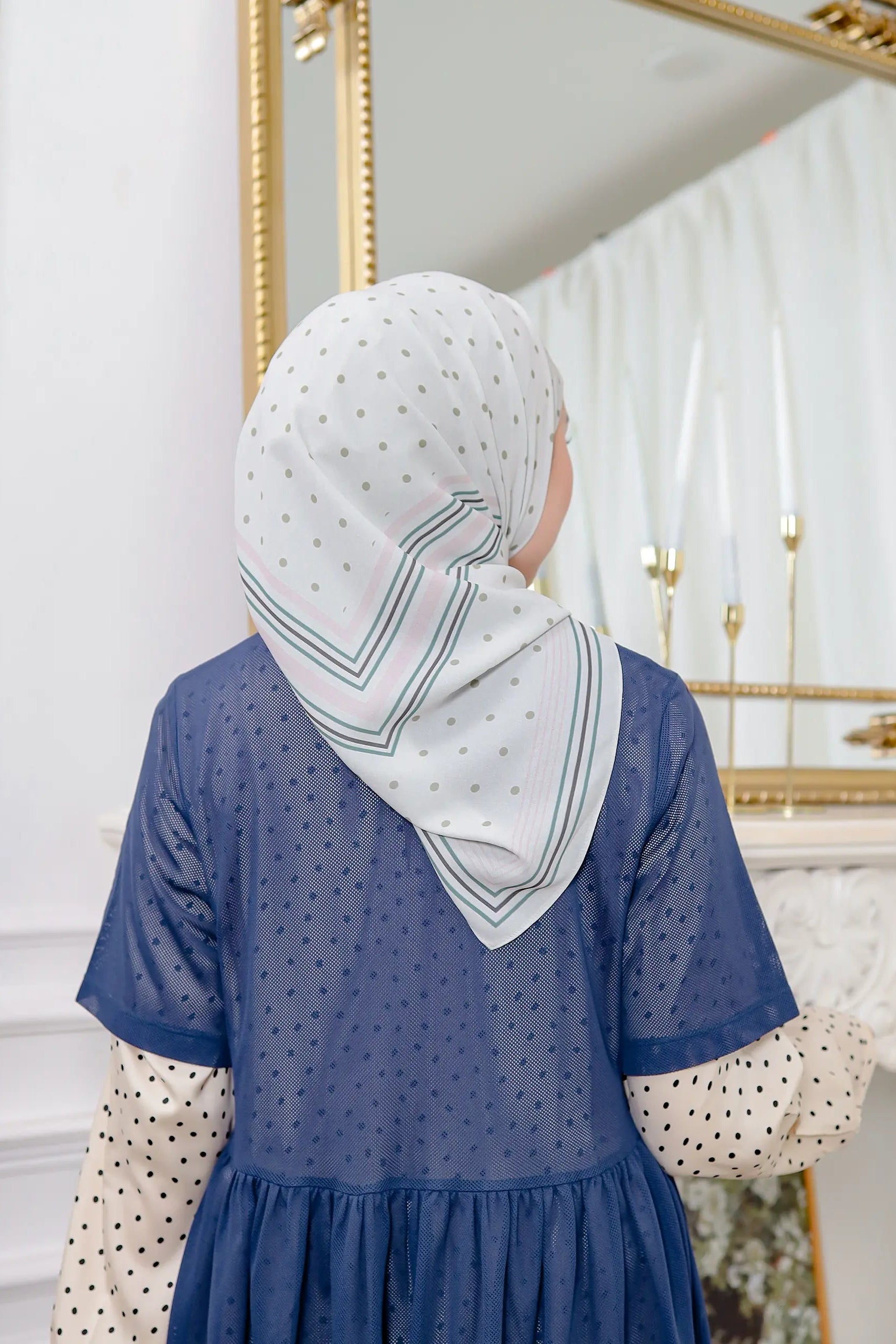 Woman wearing a blue dress and white hijab in front of a mirror.