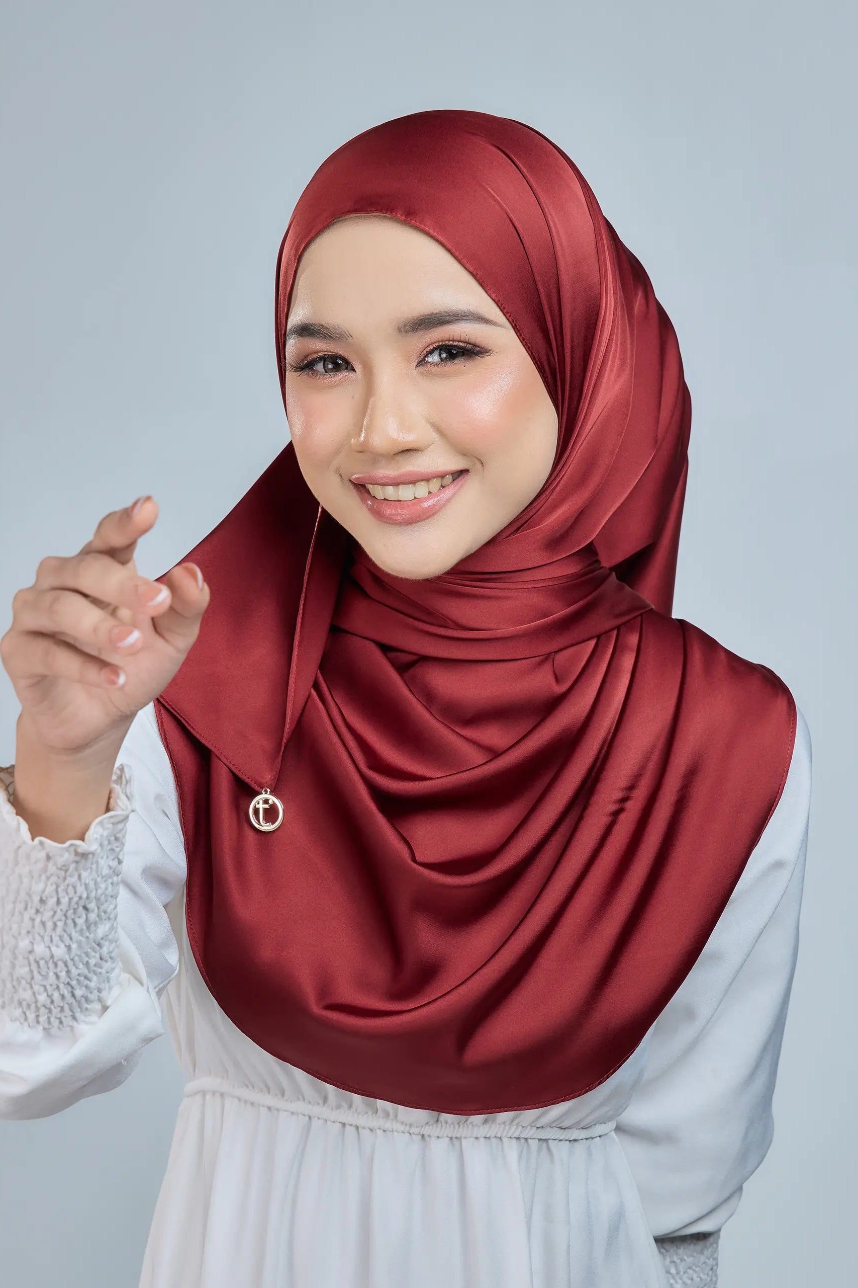Woman wearing a red hijab and white blouse against a gray background