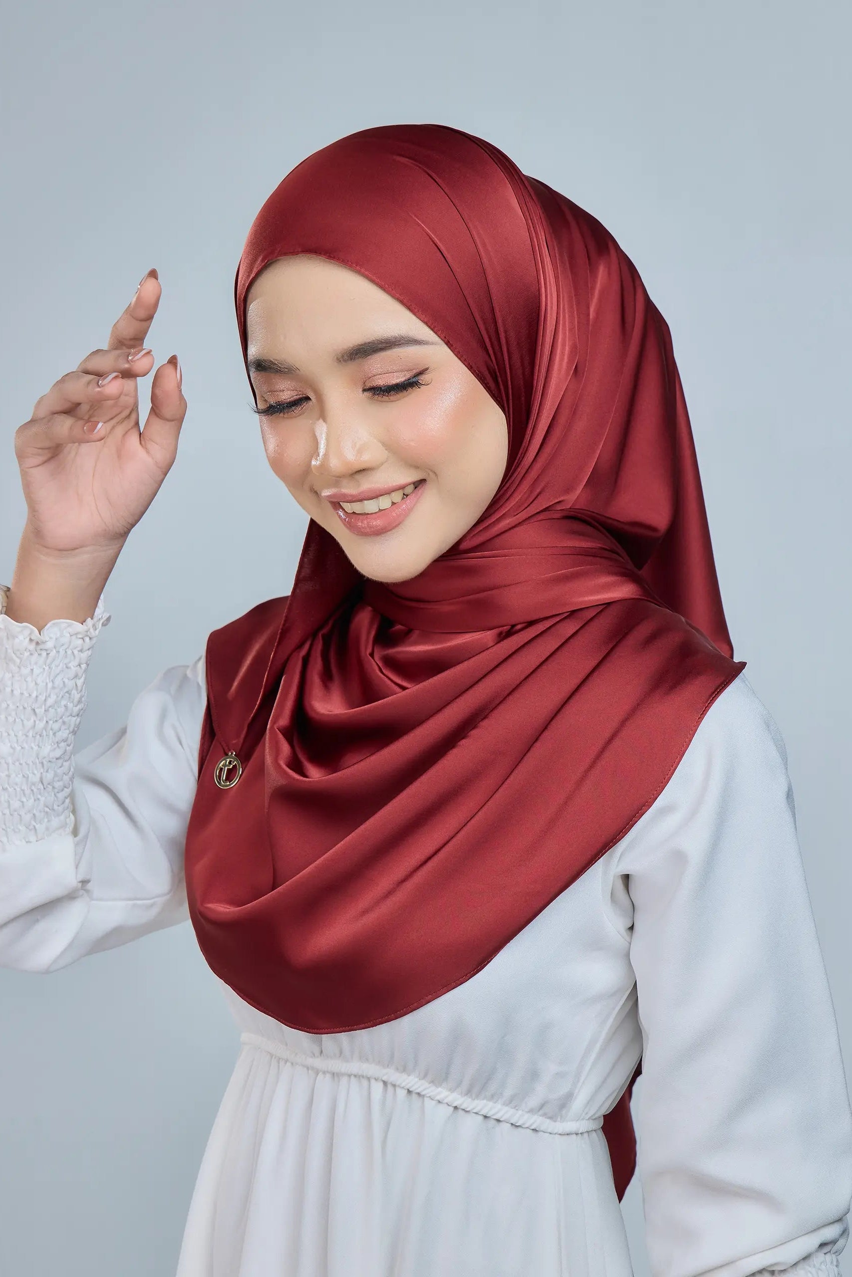 Woman wearing a red hijab and white dress against a gray background