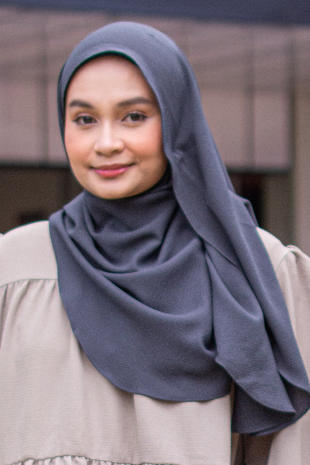 Woman wearing a gray hijab and beige dress outdoors