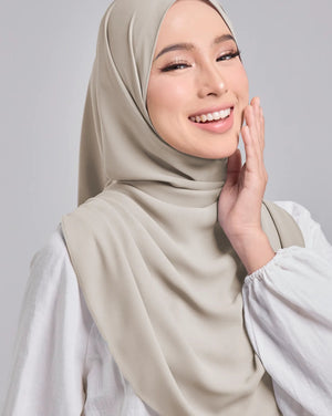Woman wearing a beige hijab and white top against a gray background
