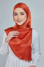 Woman wearing an orange hijab and white top on a gray background