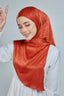 Woman wearing a rust-colored hijab and white outfit on a light gray background